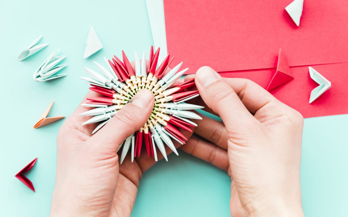 Close-up of a person's hand making the paper flower on teal background