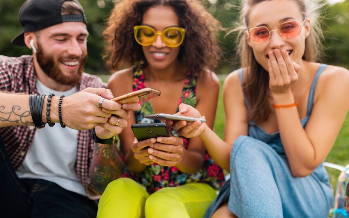 A group of diverse friends laughing and chatting together on a park bench, using the UpSwap app on their phones.