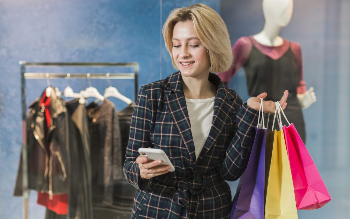 Teenager using a smartphone app to browse clothes and accessories, with a pile of clothes in the background.