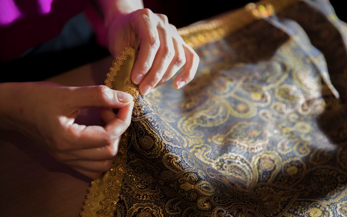 Close-up photo of Rani, a woman with a warm smile, sitting at a traditional loom weaving a colorful Tanutra textile.